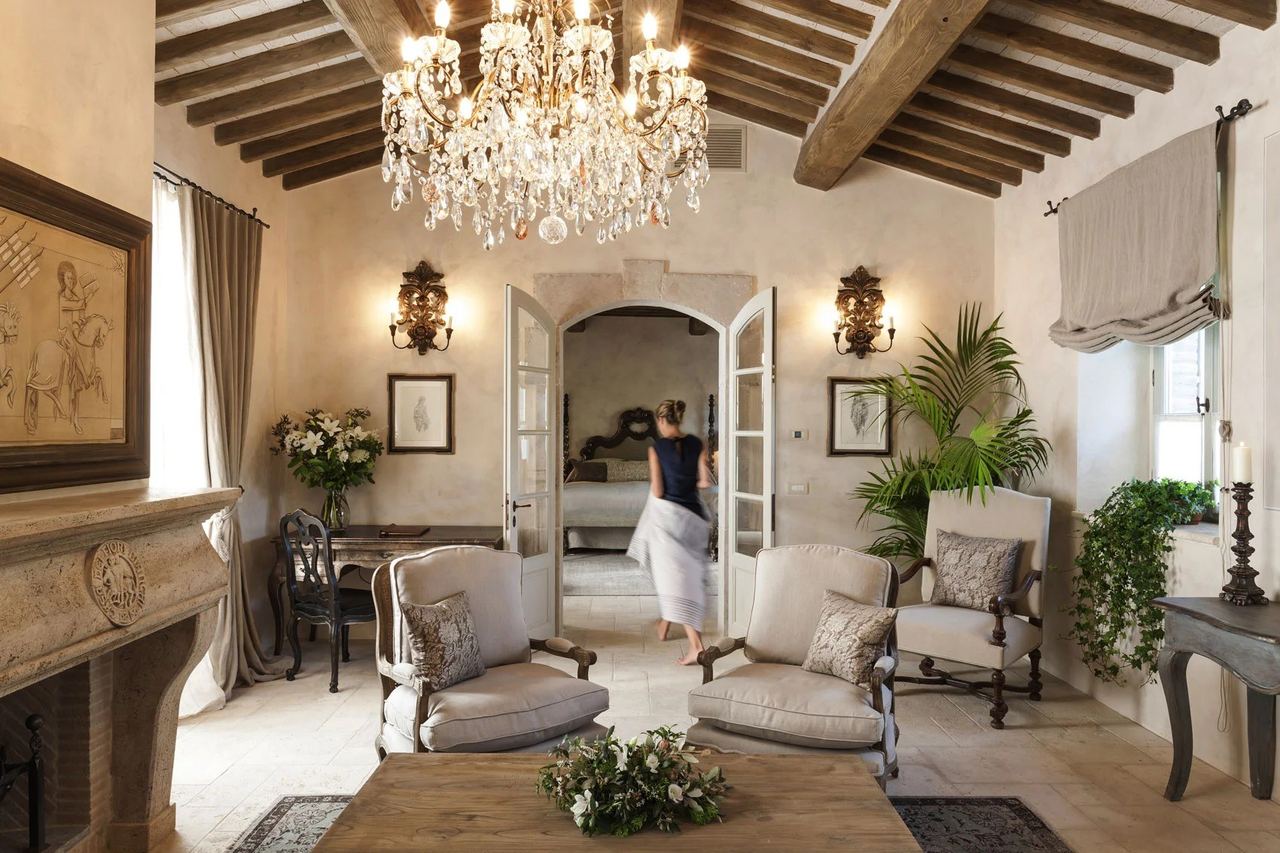 A suite sitting room at Borgo Santo Pietro, under a crystal chandelier and old oak beams
