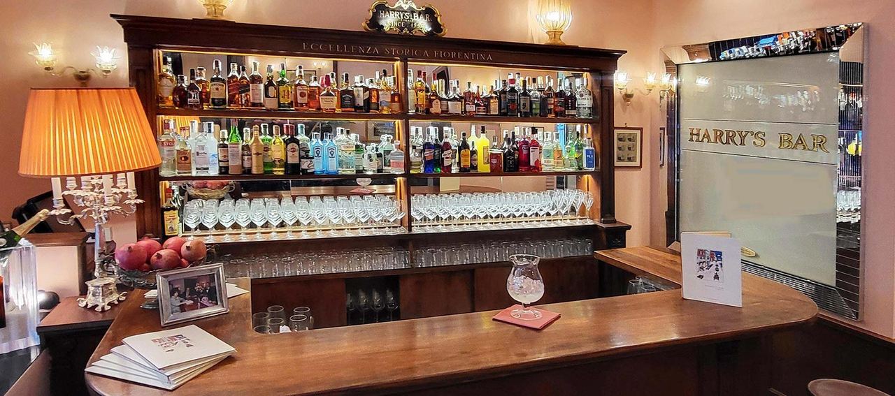 The wooden bar counter at Harry’s Bar Firenze, its back-lit shelves of bottles and glasses under a lamp