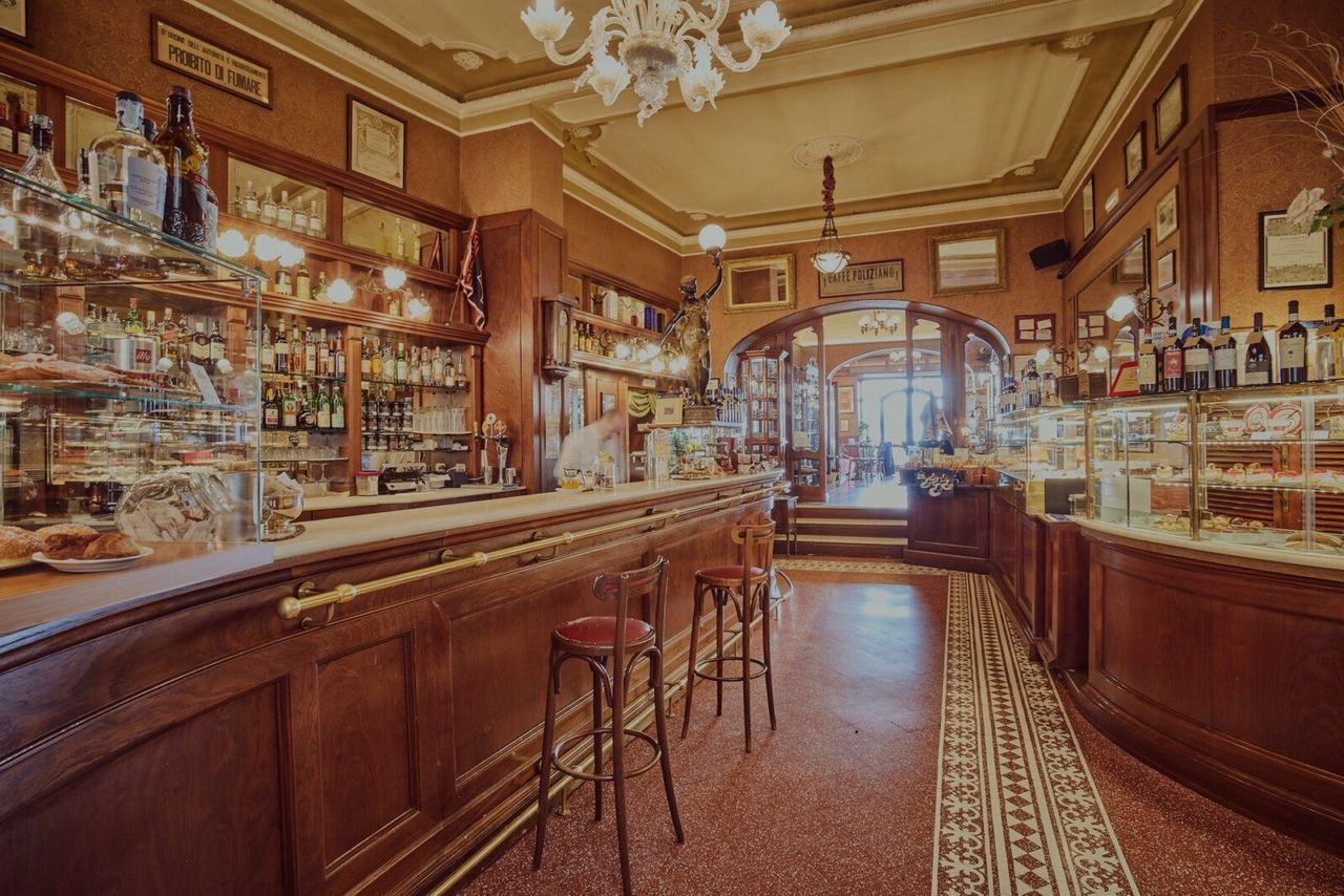 The long wooden bar and pastry counters of the Caffè Poliziano under a glass chandelier